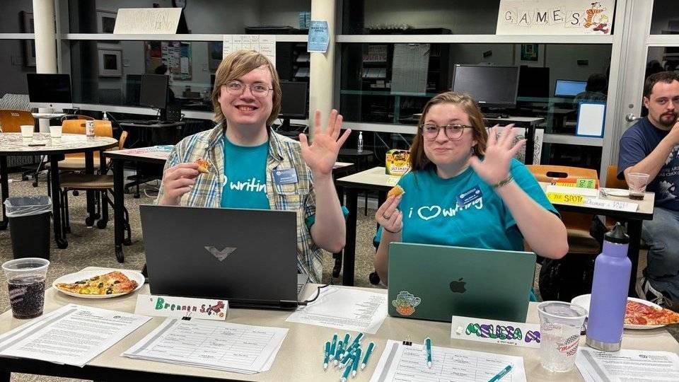 students from the writing center eating pizza in front of laptop computers while waving to the camera